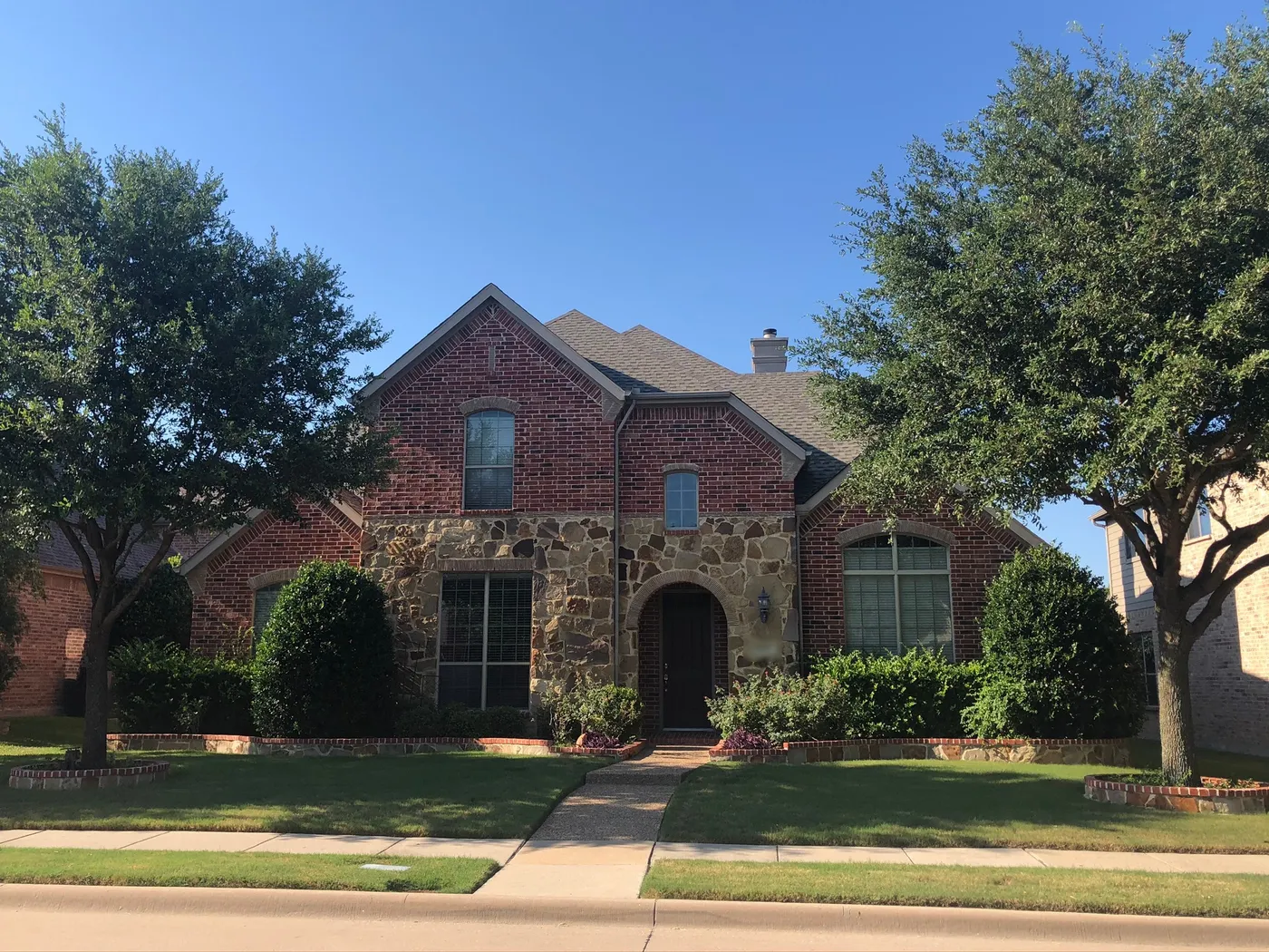 Red brick and stone two-story home with mature shade trees and a manicured lawn